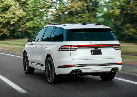 A white 2025 Lincoln Aviator® SUV is being driven away down a road lined with colorful trees. | Doggett Lincoln of Beaumont in Beaumont TX