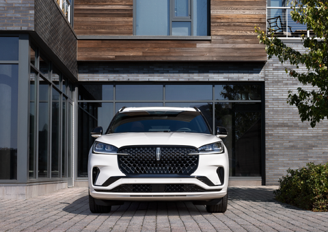 A white 2025 Lincoln Aviator® SUV is shown parked outside a modern building with gray brick and wood accents. | Doggett Lincoln of Beaumont in Beaumont TX