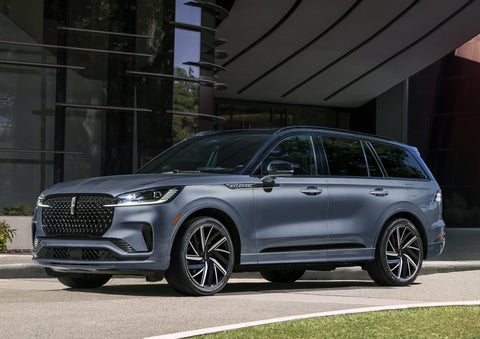 A gray 2025 Lincoln Aviator® SUV is parked outside a modern building showcasing the driver’s side of the vehicle. | Doggett Lincoln of Beaumont in Beaumont TX