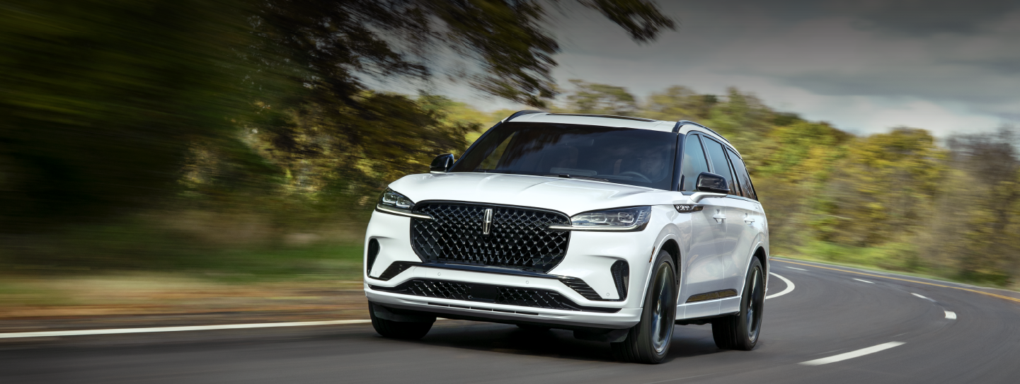 A white 2025 Lincoln Aviator® SUV is being driven down a road lined with trees. | Doggett Lincoln of Beaumont in Beaumont TX